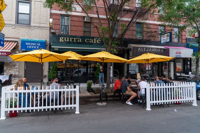 Diners sit outside on Arthur Ave, a white picket fence around the seating area